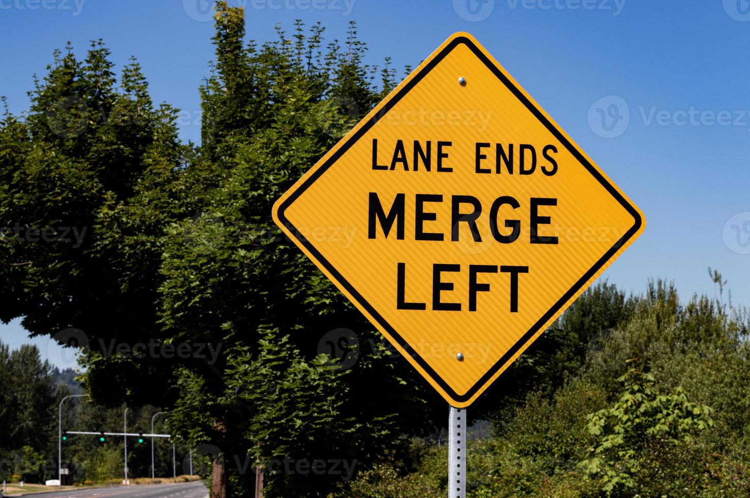 Lane ends merge left sign with trees photo