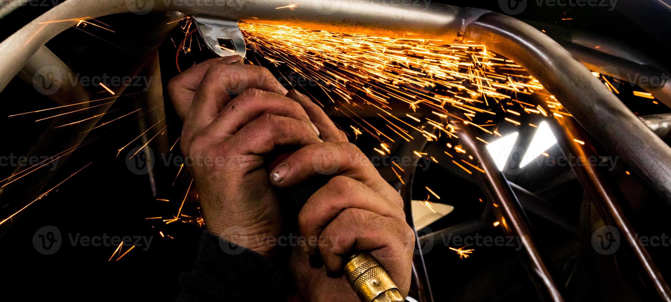 Man grinding steel tubing with a hot pneumatic grinding disc showering sparks photo