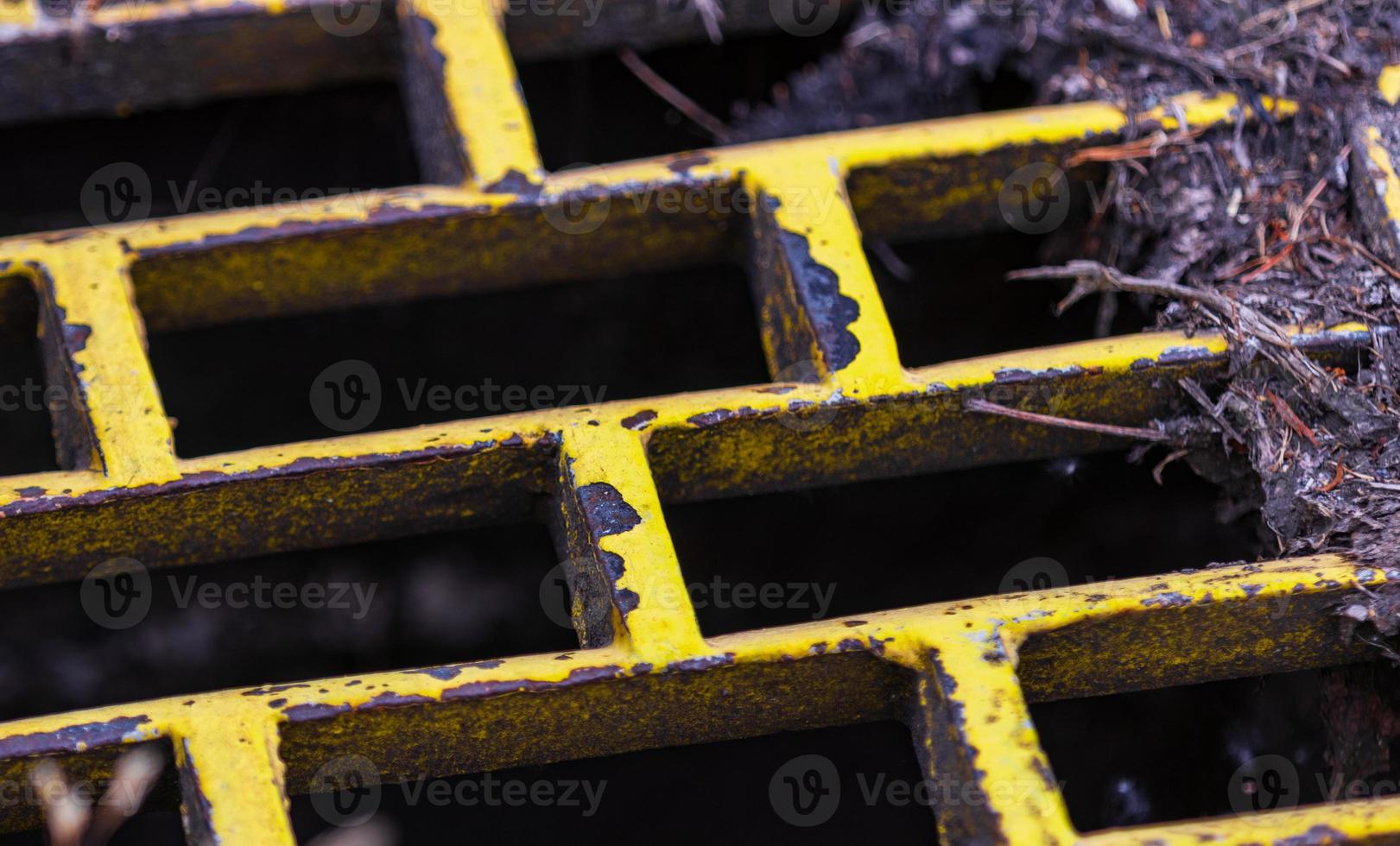 Yellow rusty iron storm drain with dried leaves and twigs photo