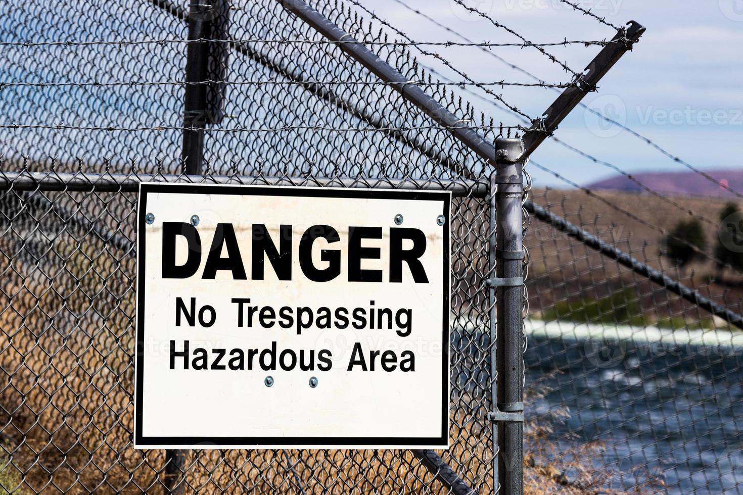 Dangerous no trespassing hazardous ares white sign on a barbed wire chain link fence photo