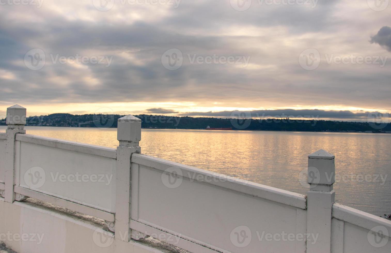 Cloudy sunrise as seen over the rail of a wooden foot bridge overlooking a harbor photo
