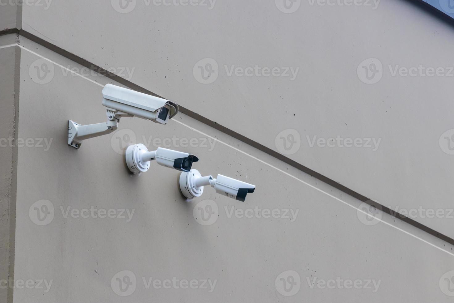 3 security cameras in a row on a brown building wall photo