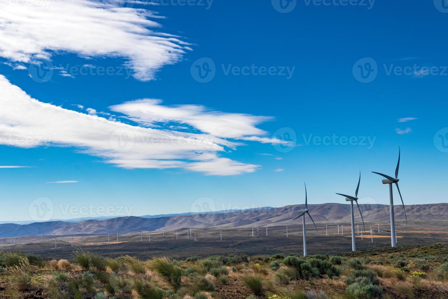 Green sustainable energy windmill power turbine electricity generators on rolling hills with clouds and blue sky above photo