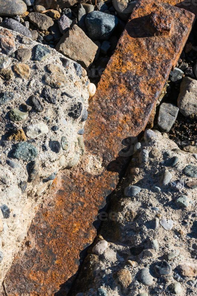 Rusty iron bar impregnated between rocky concrete blocks photo