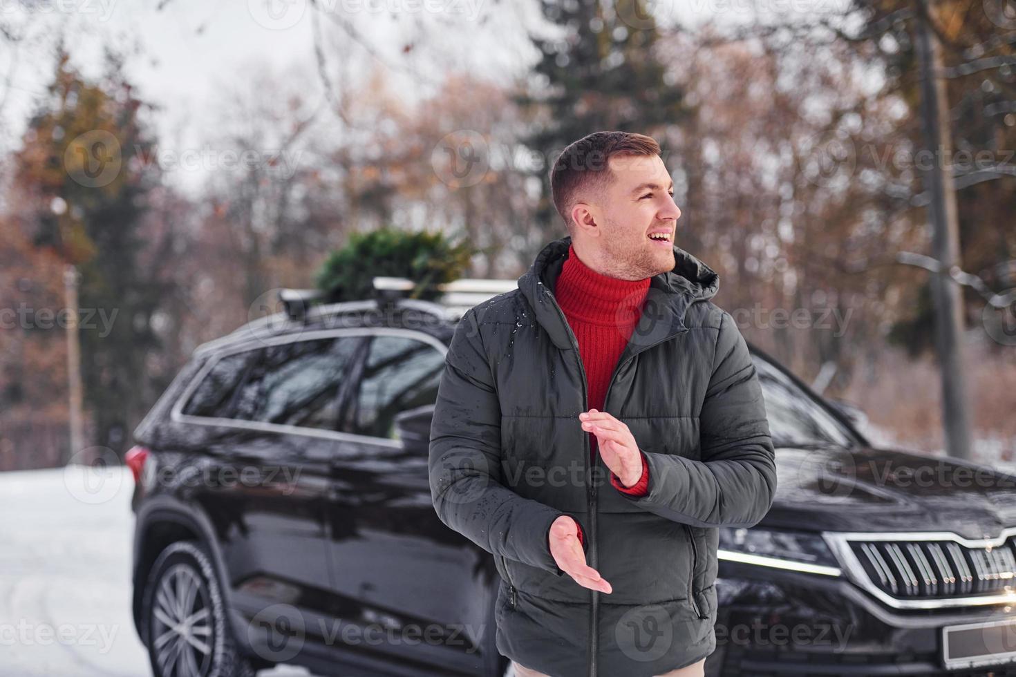 Man with little green fir is outdoors near his car. Conception of holidays photo