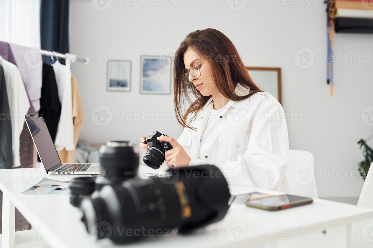 Female photographer in casual clothes is working indoors at daytime photo