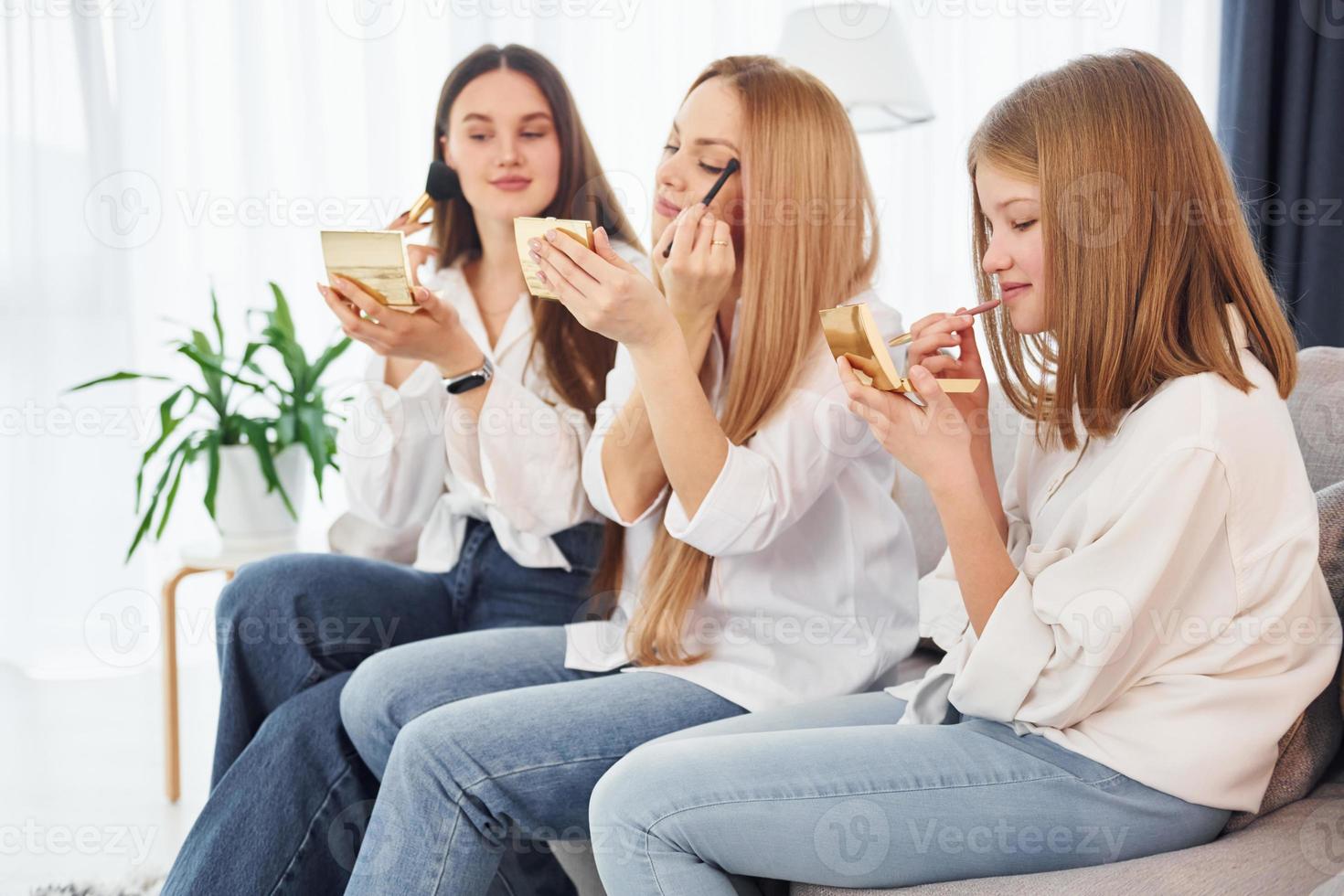 Teaching how to do make up. Young mother with her two daughters at home at daytime photo