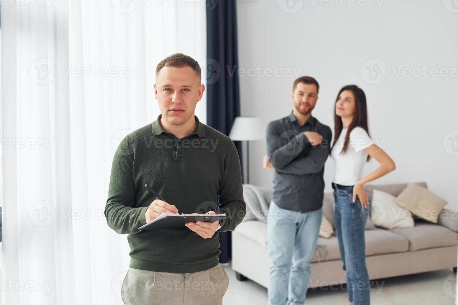 Salesman helps young couple in choosing an apartment. Conception of business and rent photo