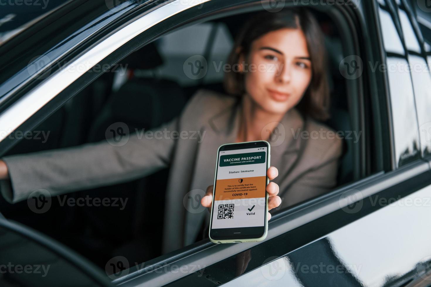 Holding vaccine passport. Woman testing new car. Sitting indoors in modern automobile photo