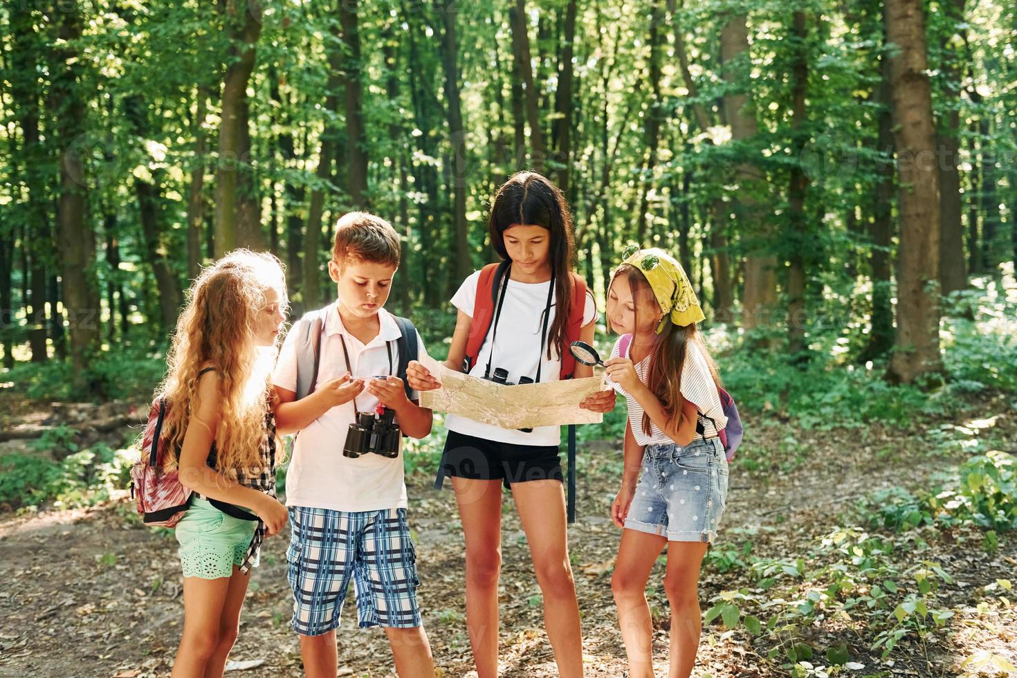 Using map to find a way. Kids strolling in the forest with travel equipment photo