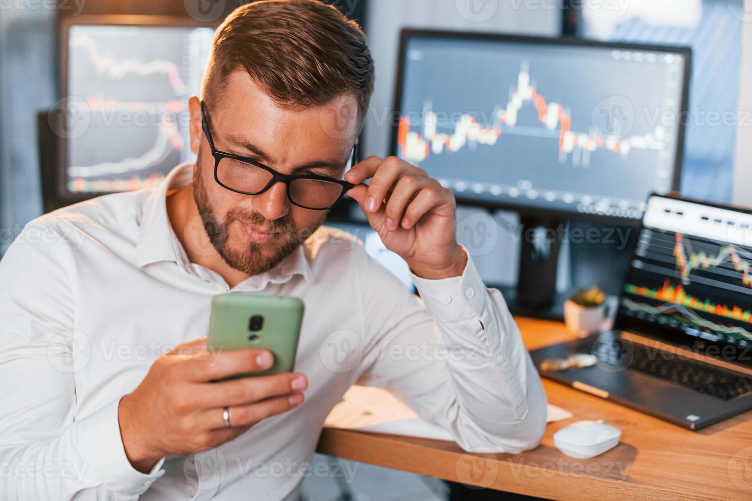 With phone in hands. Young businessman in formal clothes is in office with multiple screens photo