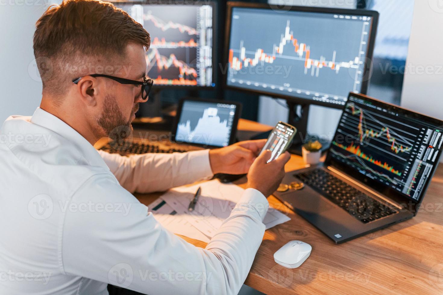 Side view. Young businessman in formal clothes is in office with multiple screens photo