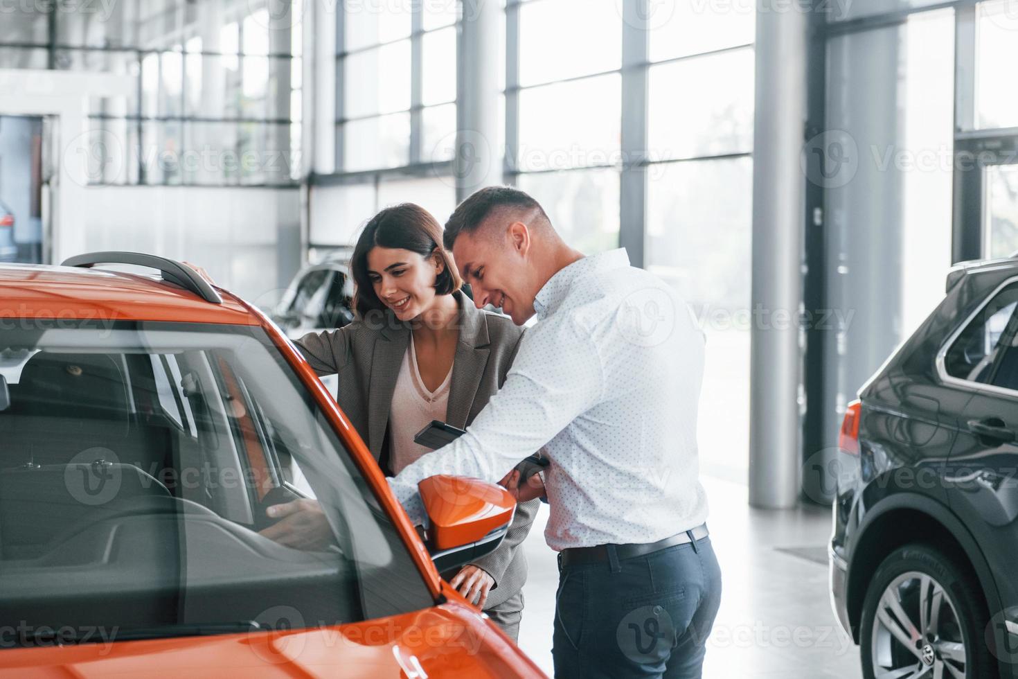 Orange colored car. Man in formal wear helping customer with choice of the automobile photo