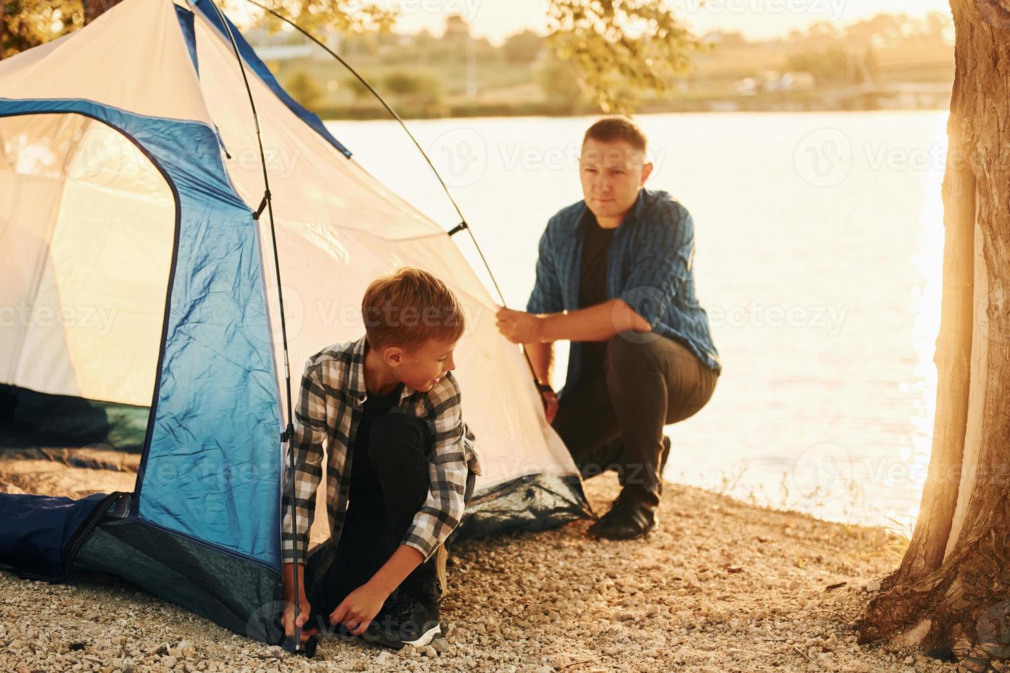 Father and son installing tent outdoors near the lake photo