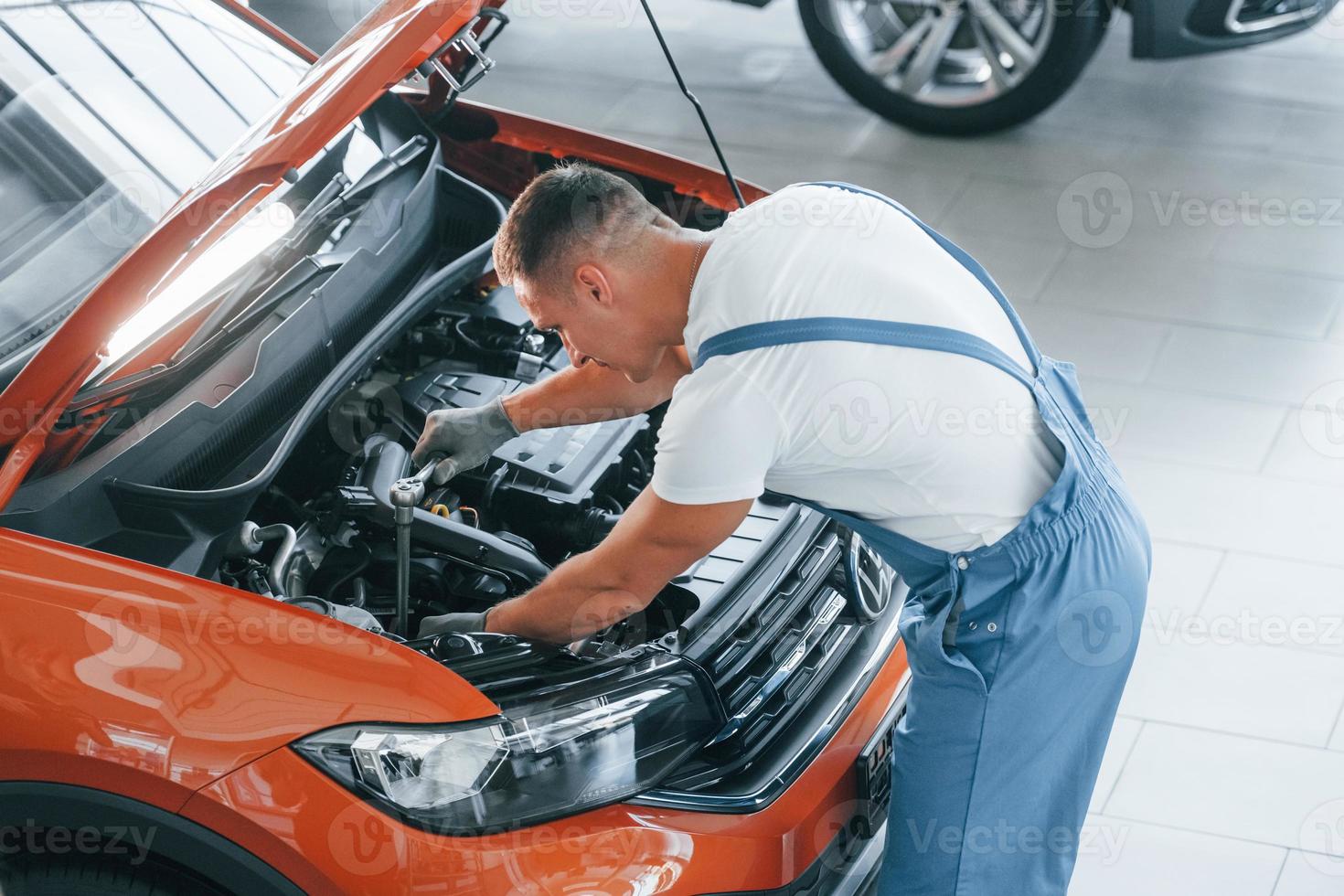 View from above. Man in uniform is repairing broken automobile indoors photo