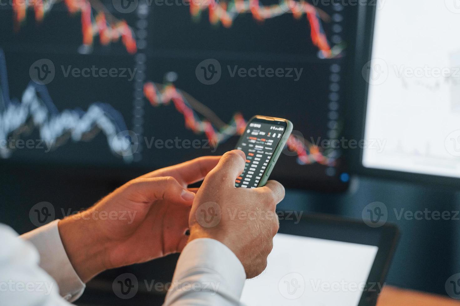 Busy young businessman in formal clothes is in office with multiple screens photo