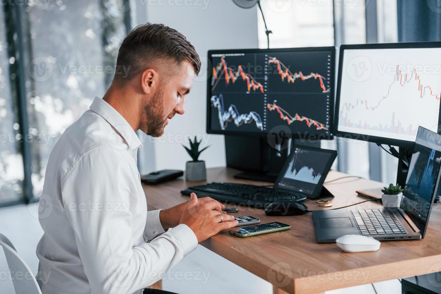 Focusing on the work. Young businessman in formal clothes is in office with multiple screens photo
