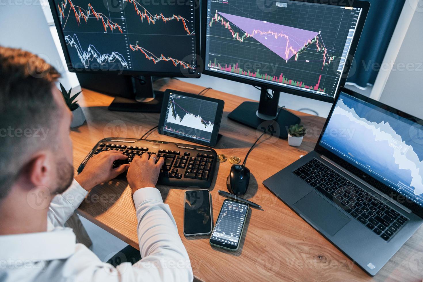 Close up view. Young businessman in formal clothes is in office with multiple screens photo