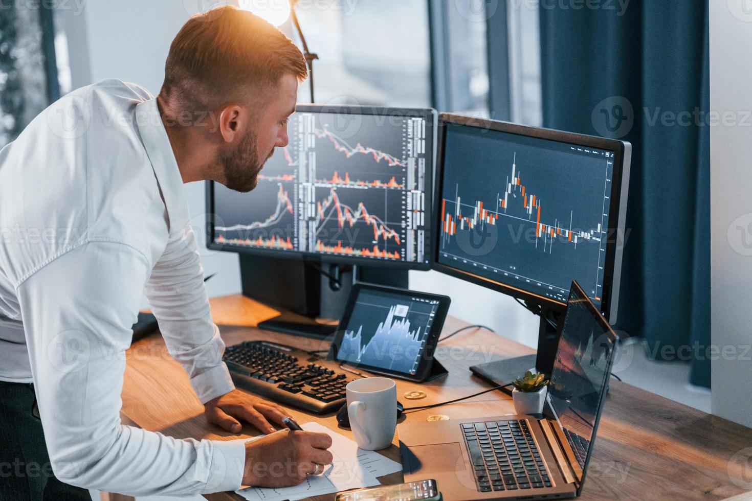 Near the table. Young businessman in formal clothes is in office with multiple screens photo