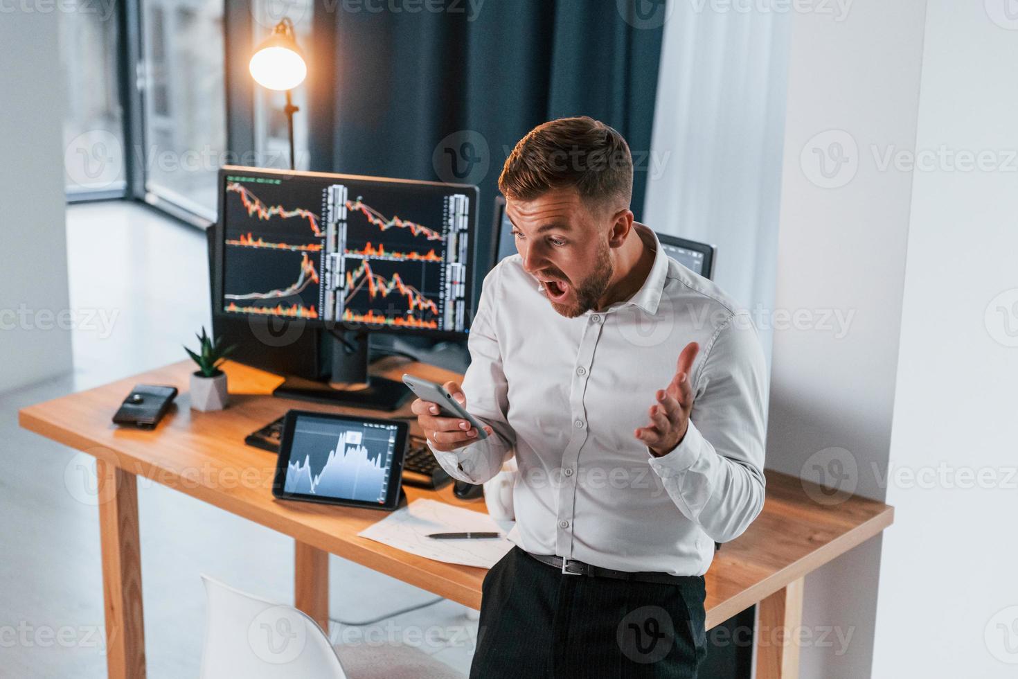 Near the table. Young businessman in formal clothes is in office with multiple screens photo