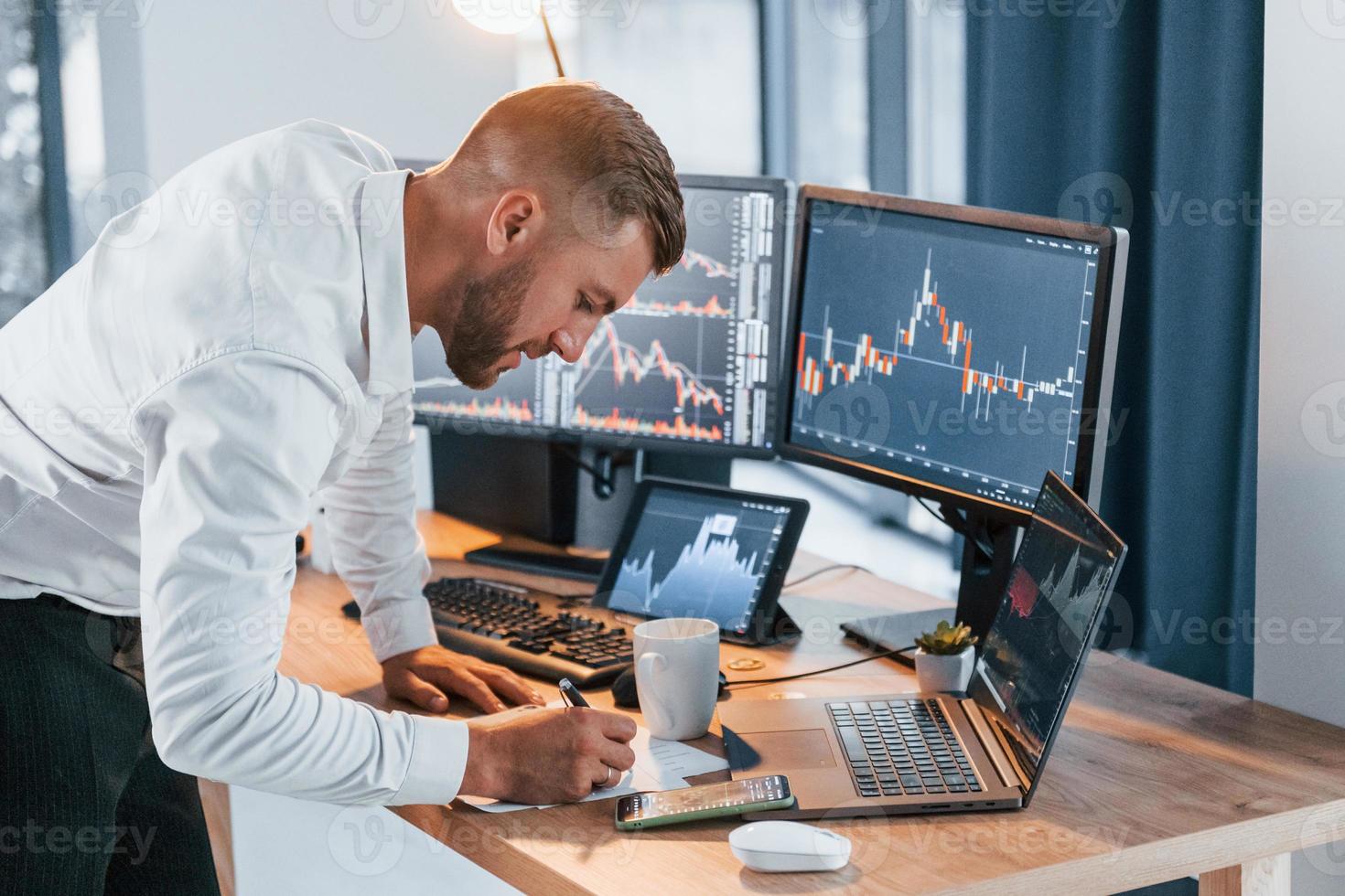 Near the table. Young businessman in formal clothes is in office with multiple screens photo