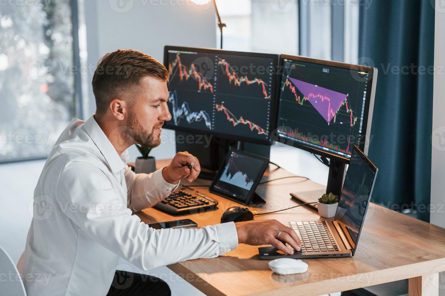 Using laptop. Young businessman in formal clothes is in office with multiple screens photo