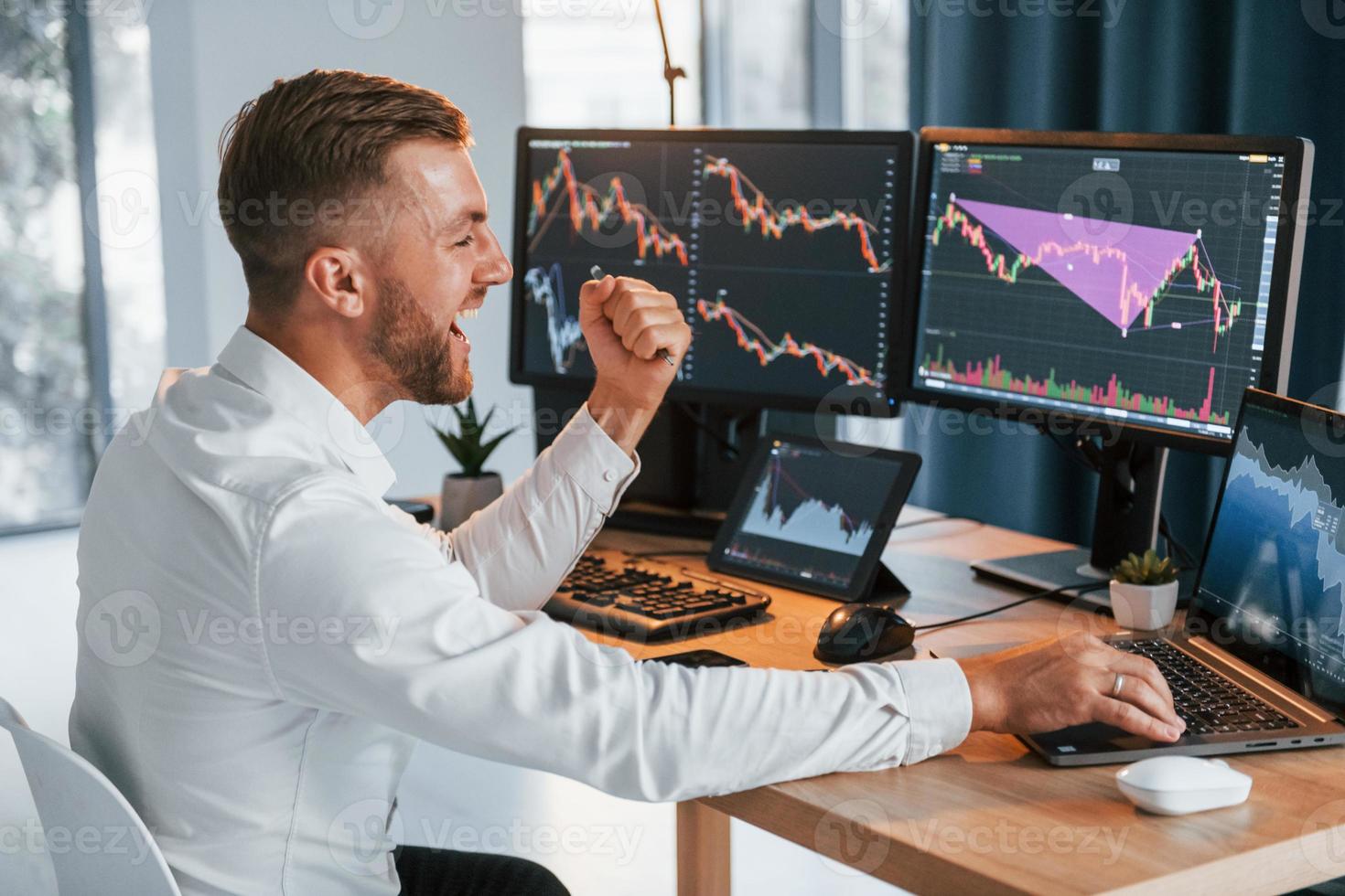 Using laptop. Young businessman in formal clothes is in office with multiple screens photo