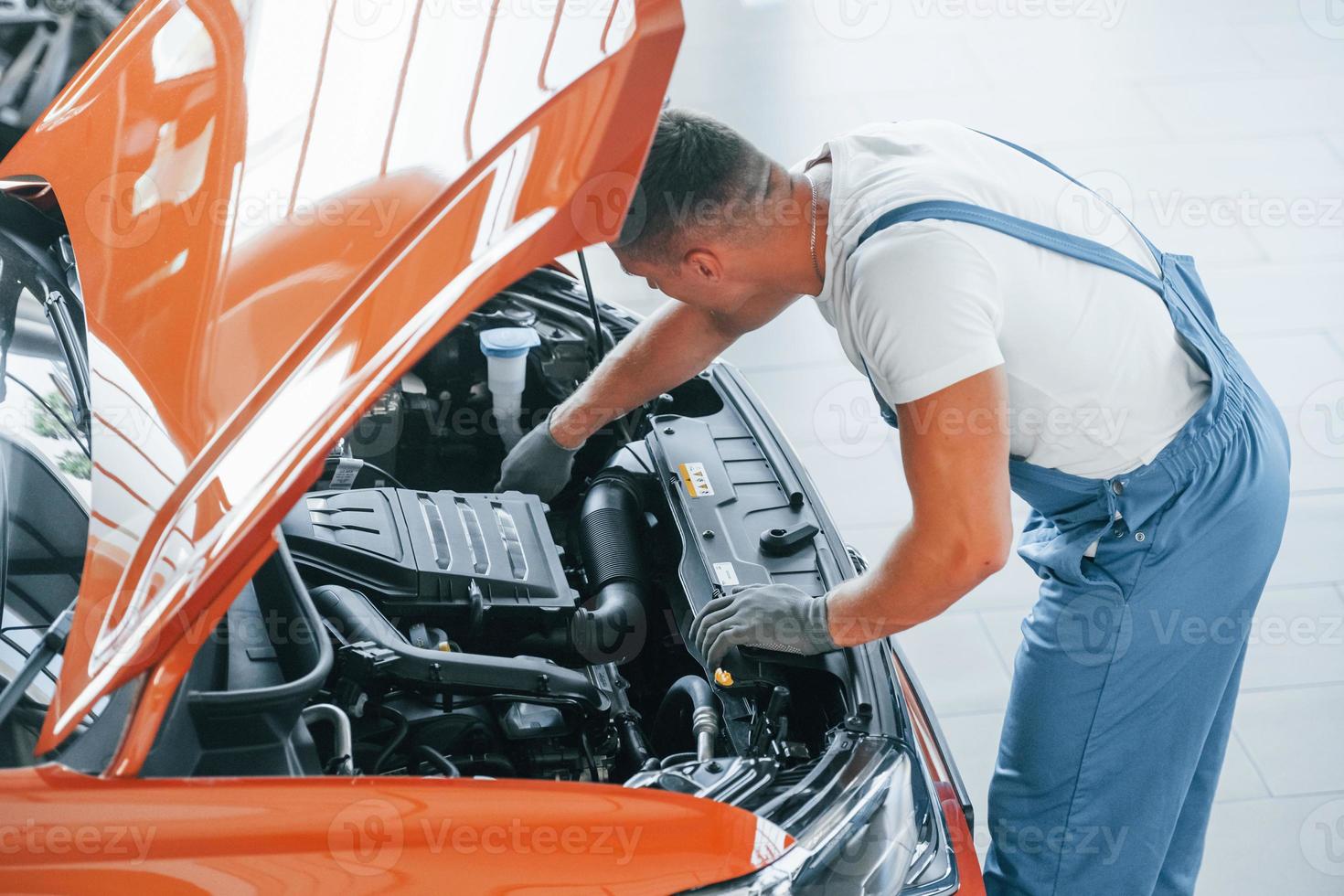 View from above. Man in uniform is repairing broken automobile indoors photo