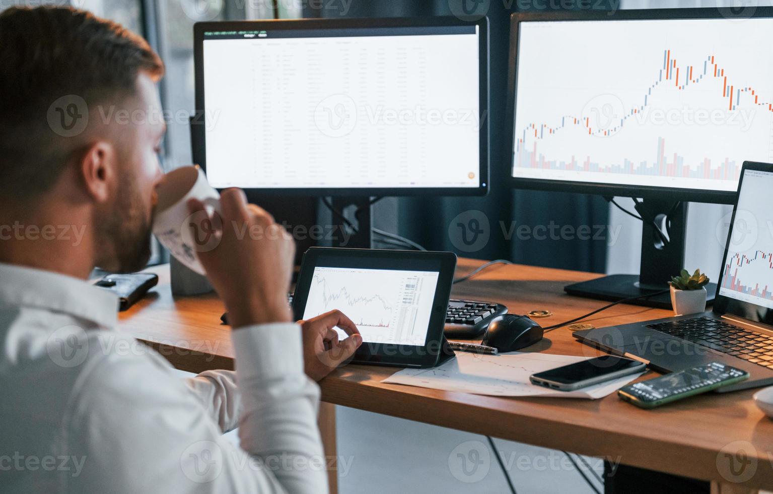 Looking at information. Young businessman in formal clothes is in office with multiple screens photo