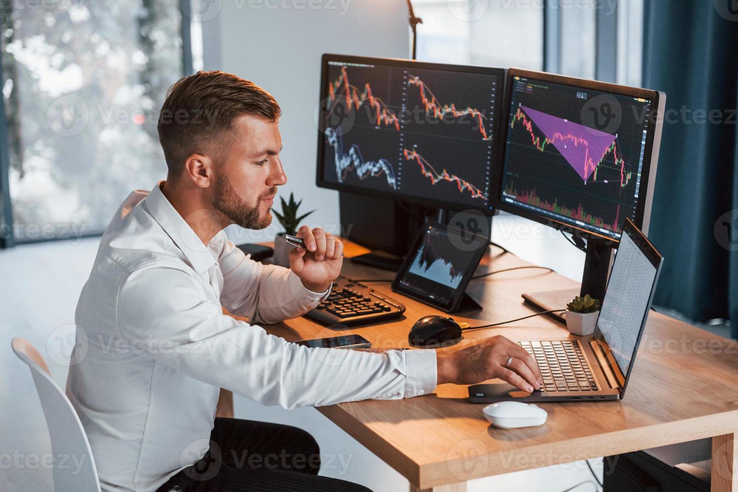 Using laptop. Young businessman in formal clothes is in office with multiple screens photo