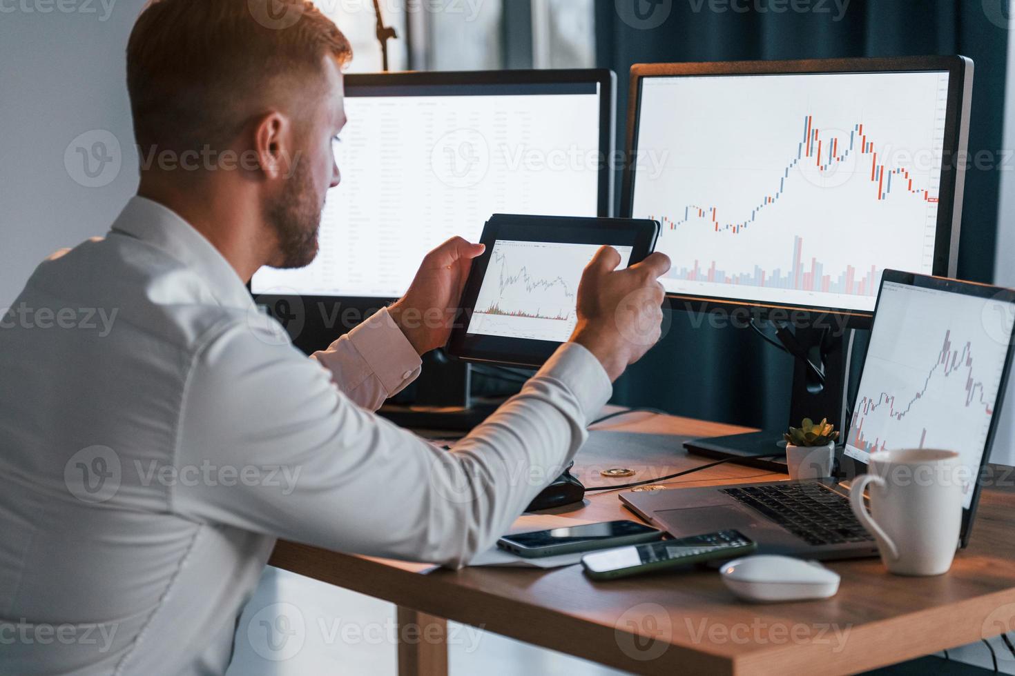 Looking at information. Young businessman in formal clothes is in office with multiple screens photo