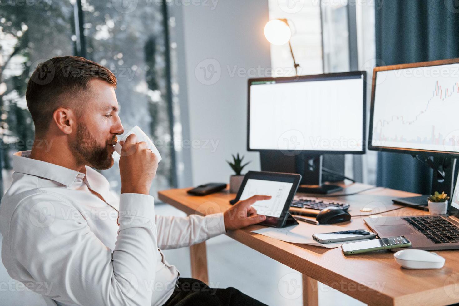 Busy day. Young businessman in formal clothes is in office with multiple screens photo