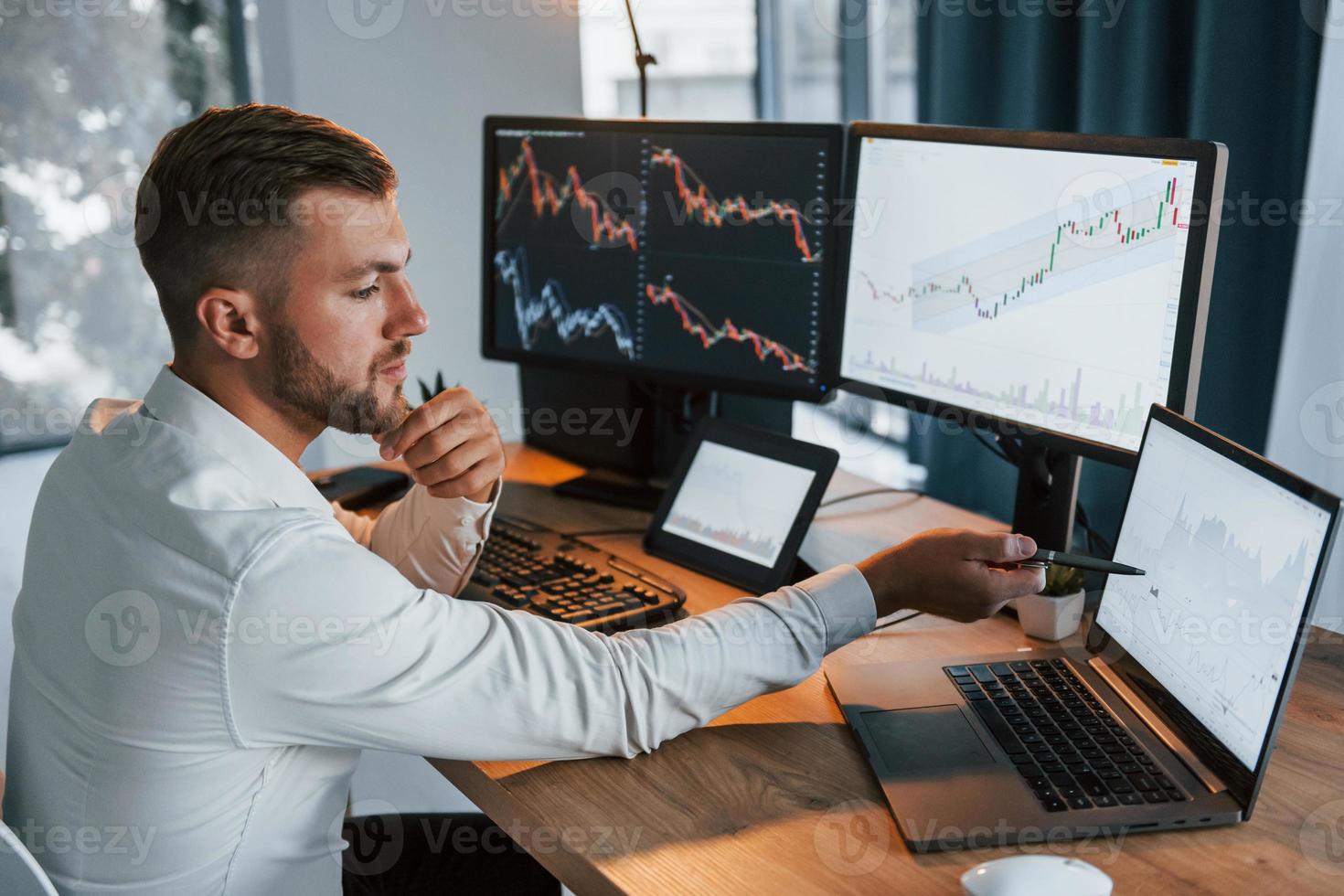 Young businessman in formal clothes is in office with multiple screens. Conception of exchange photo