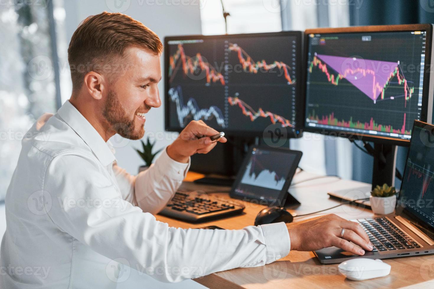 Using laptop. Young businessman in formal clothes is in office with multiple screens photo