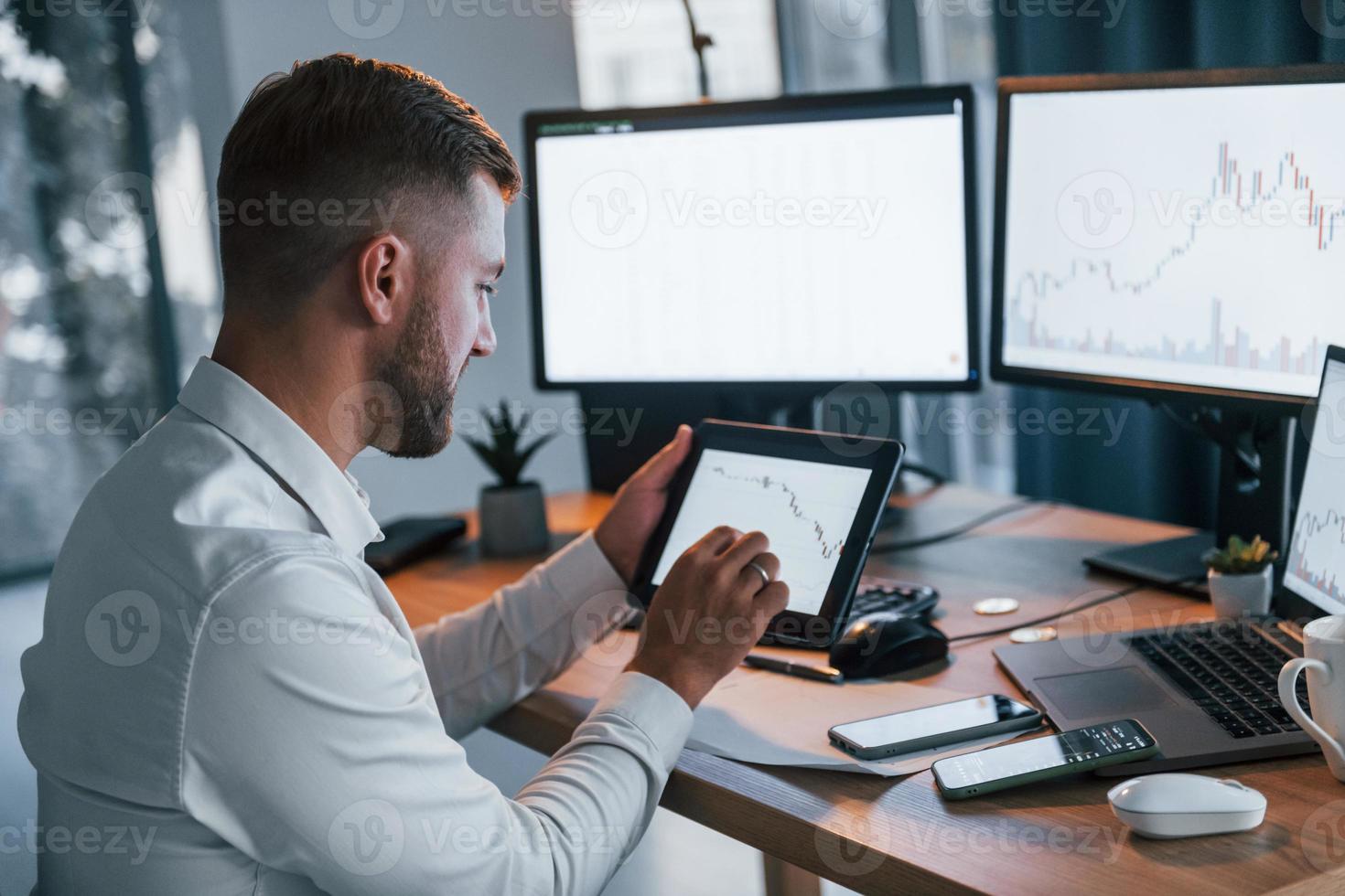 Modern technologies. Young businessman in formal clothes is in office with multiple screens photo