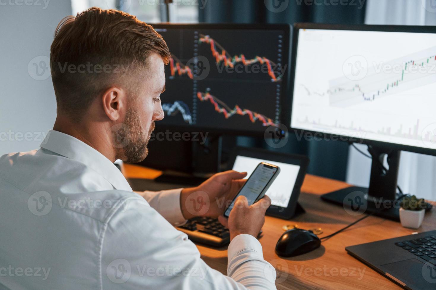 Young businessman in formal clothes is in office with multiple screens. Conception of exchange photo