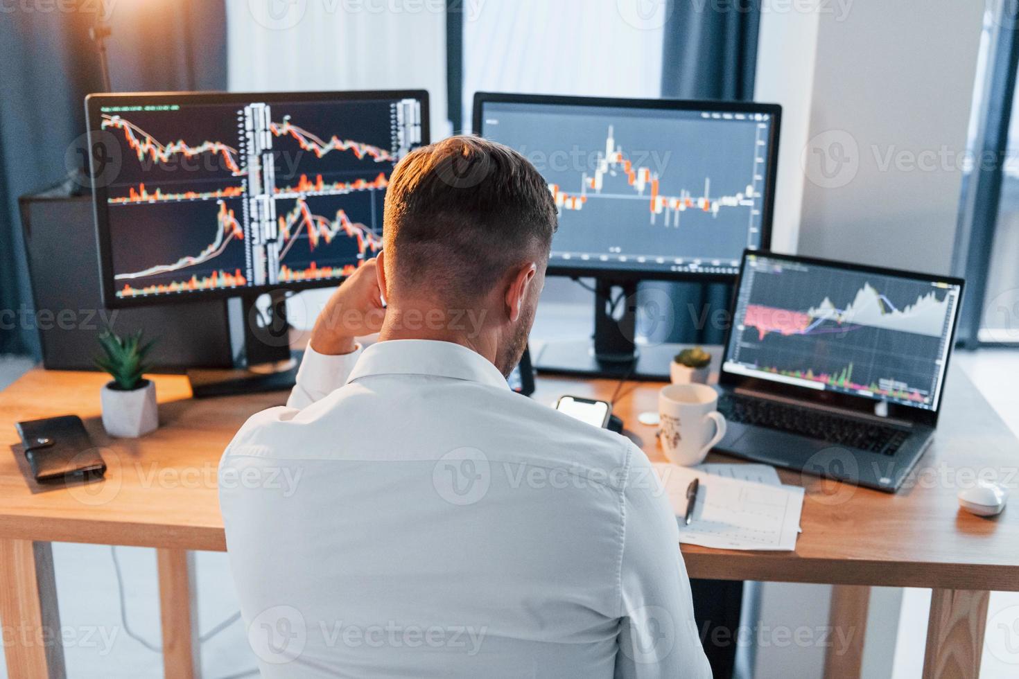 Hard working. Young businessman in formal clothes is in office with multiple screens photo