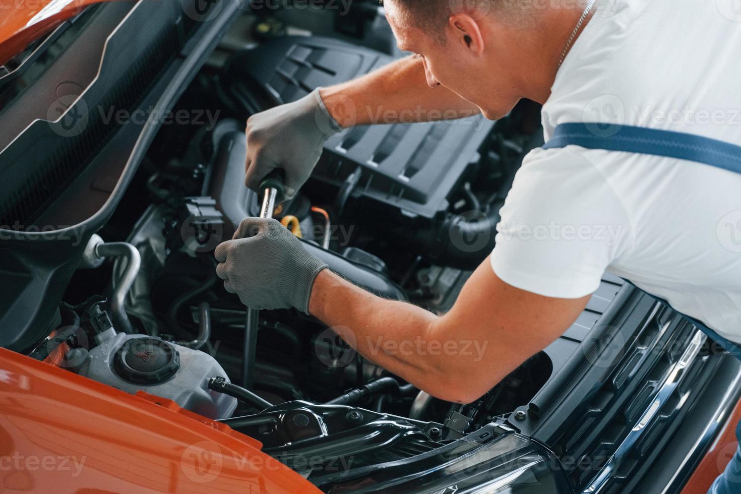View from above. Man in uniform is repairing broken automobile indoors photo