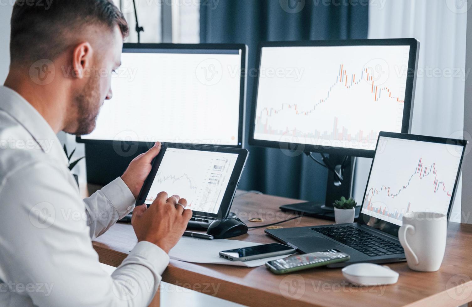 Modern technologies. Young businessman in formal clothes is in office with multiple screens photo
