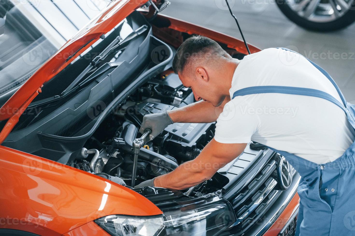 View from above. Man in uniform is repairing broken automobile indoors photo