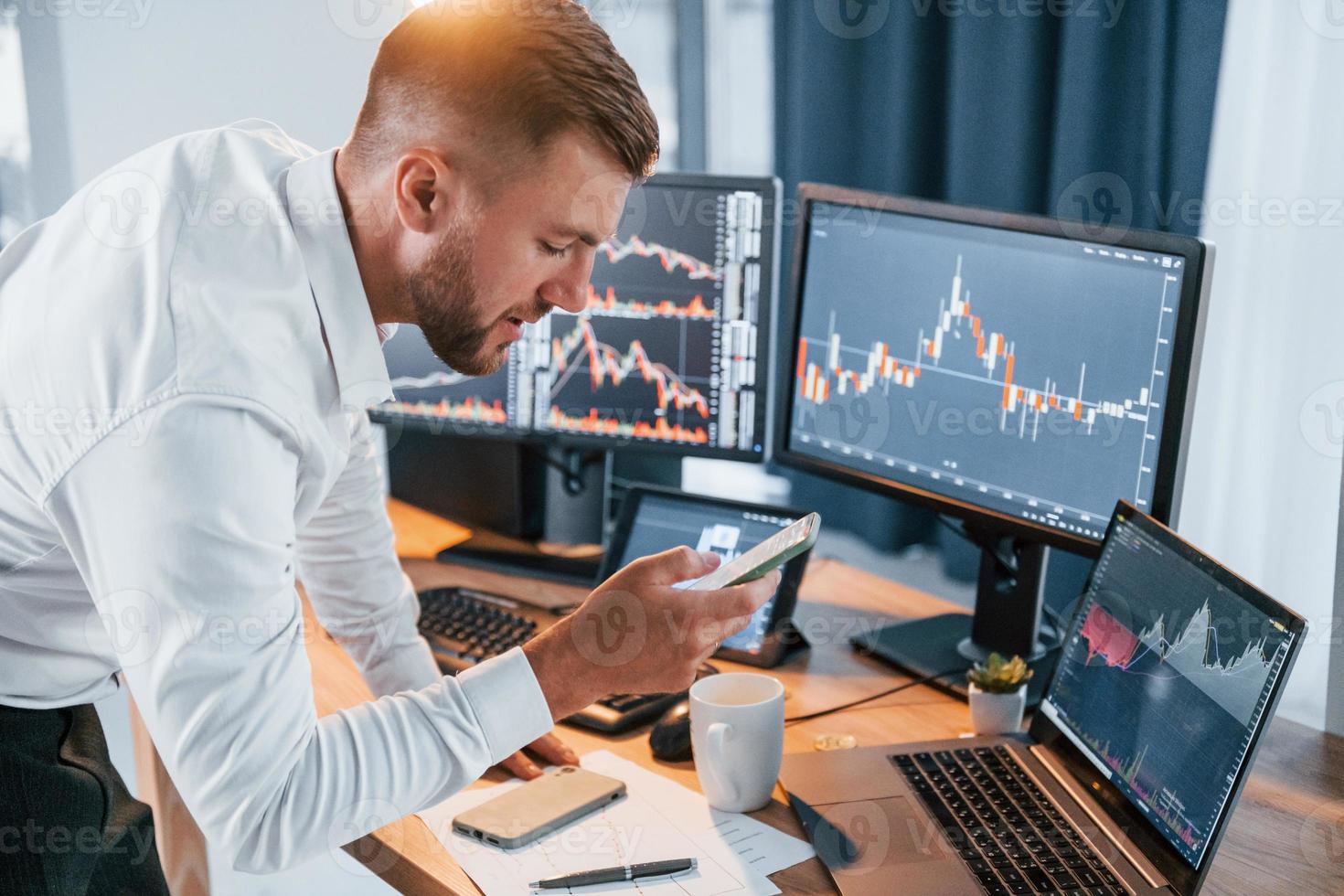 Near the table. Young businessman in formal clothes is in office with multiple screens photo