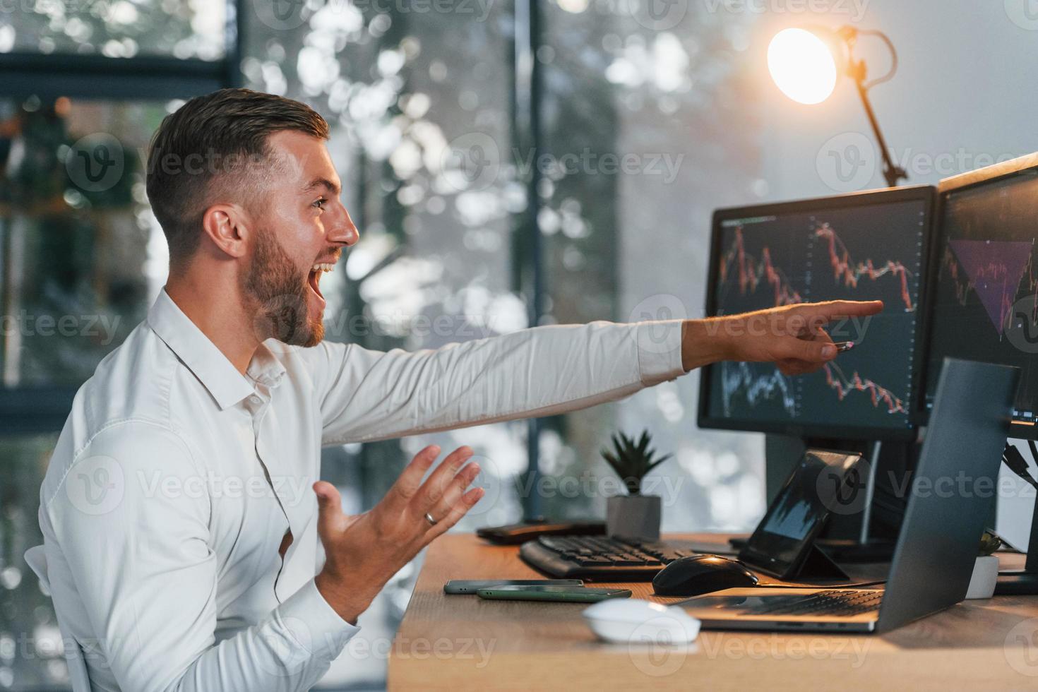 Successful young businessman in formal clothes is in office with multiple screens photo