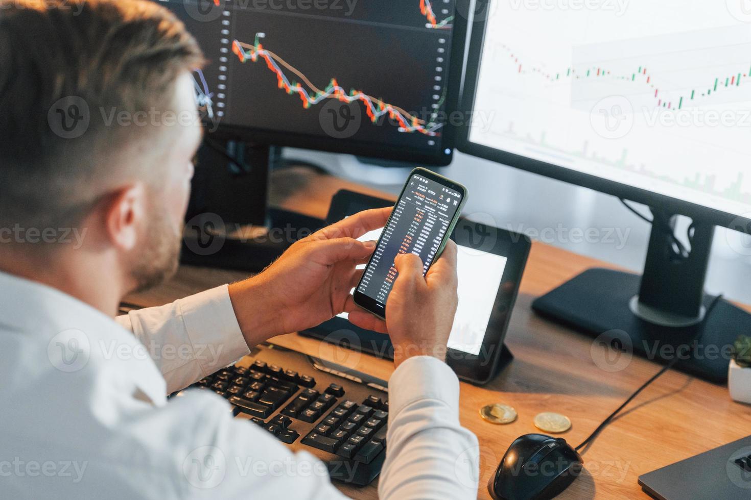Graphs is going down. Young businessman in formal clothes is in office with multiple screens photo