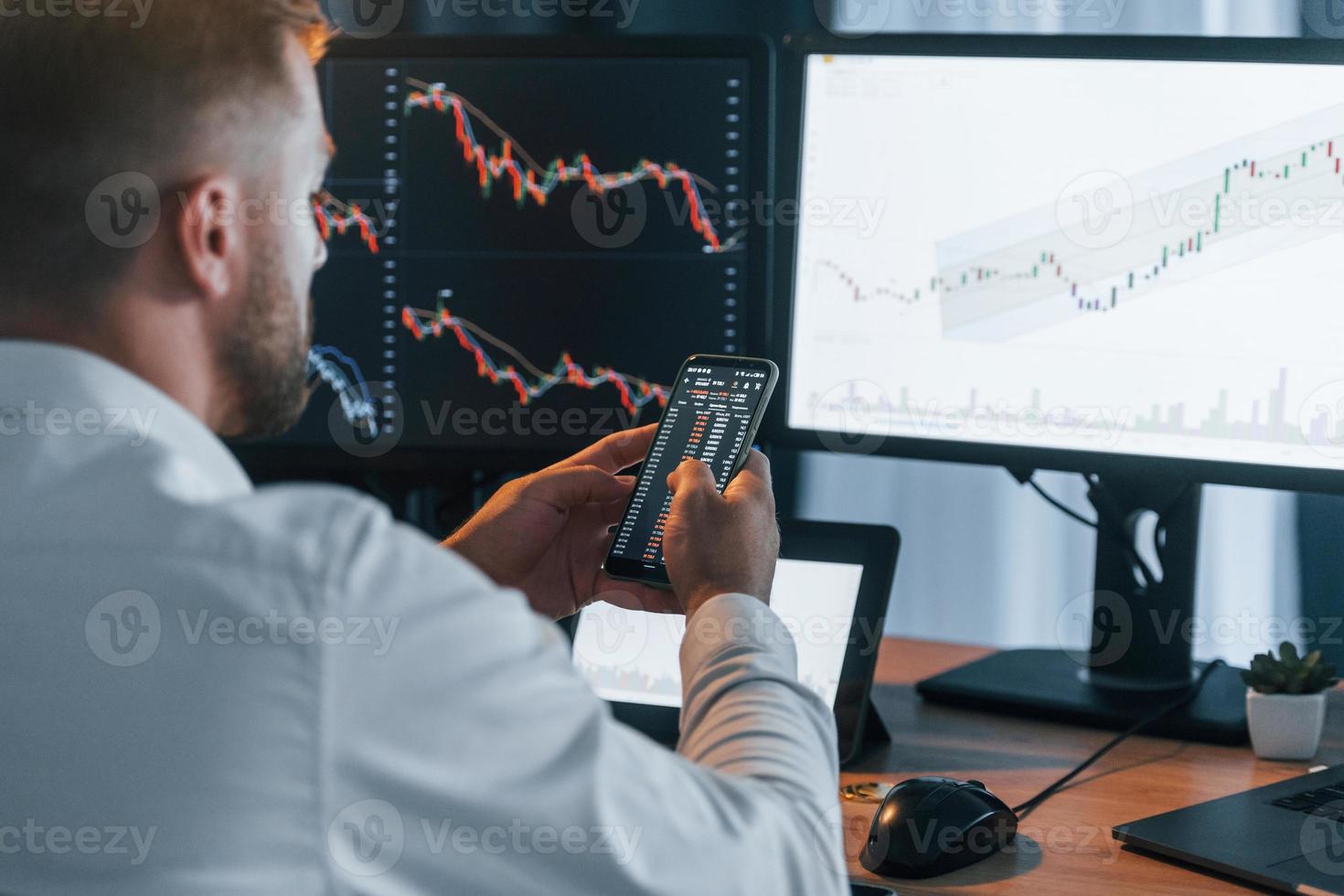 Graphs is going down. Young businessman in formal clothes is in office with multiple screens photo