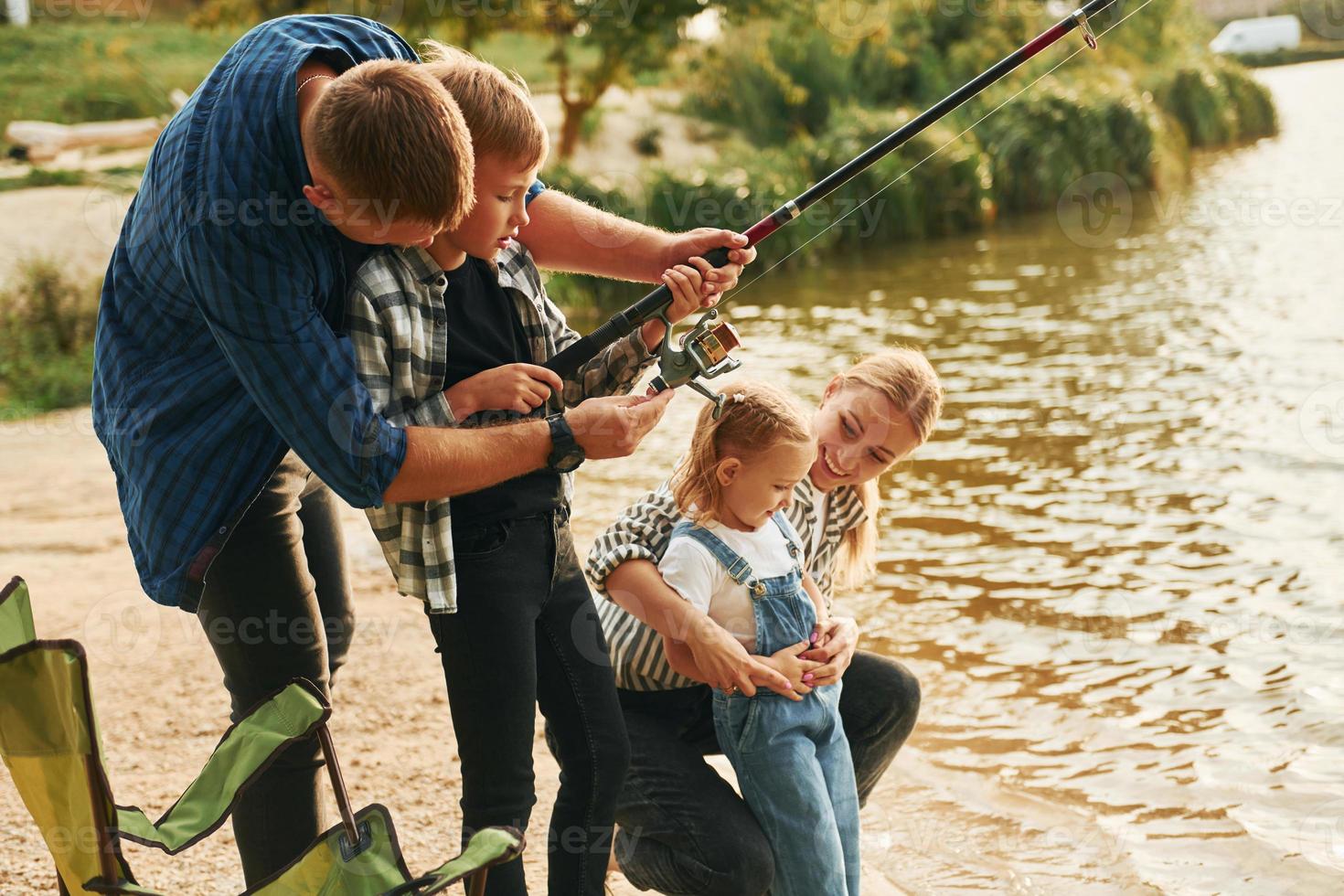 Learning to fishing. Father and mother with son and daughter together outdoors at summertime photo