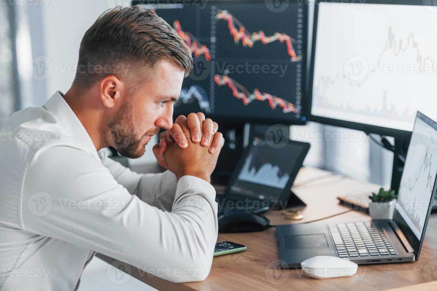 Risky job. Young businessman in formal clothes is in office with multiple screens photo