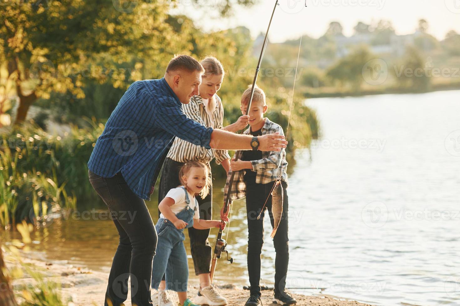 Weekend activities. Father and mother with son and daughter on fishing together outdoors at summertime photo