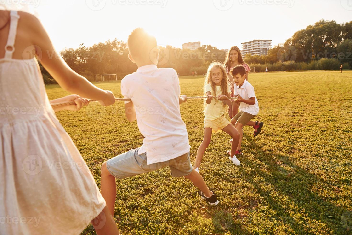 Playing tug of war. Group of happy kids is outdoors on the sportive field at daytime photo