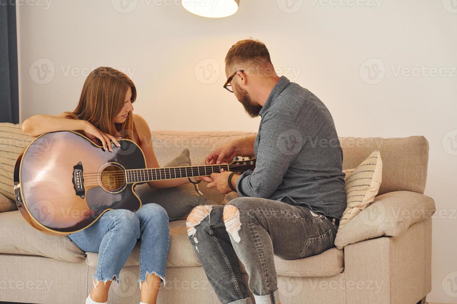 profesor de guitarra que muestra cómo tocar el instrumento a una mujer joven foto