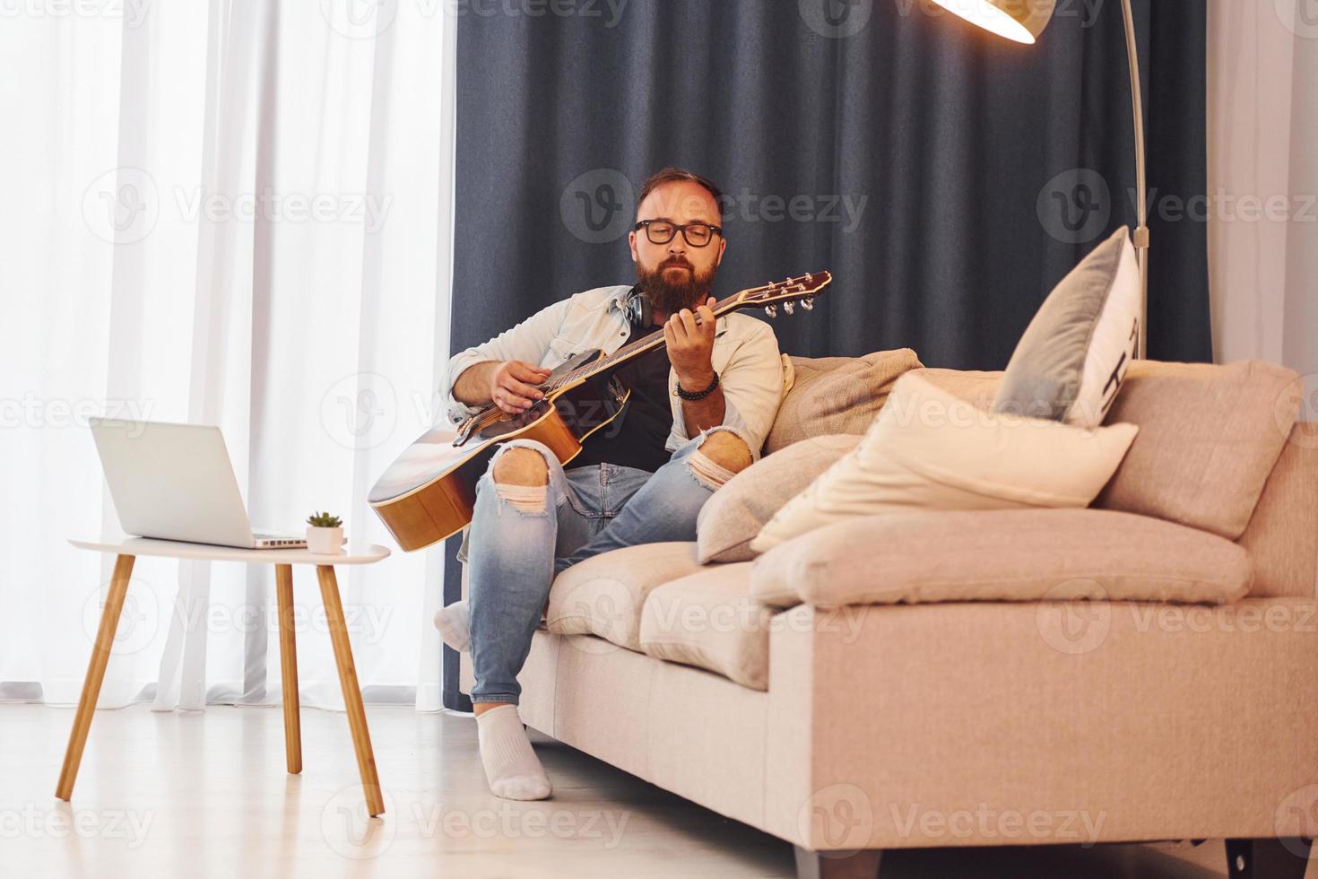 sentirse tranquilo. el hombre con ropa informal y con guitarra acústica está en el interior foto